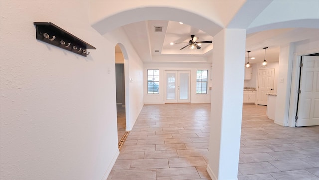 foyer entrance with baseboards, visible vents, a raised ceiling, arched walkways, and ceiling fan