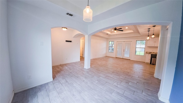 unfurnished room featuring light wood-type flooring, visible vents, a tray ceiling, ceiling fan, and arched walkways
