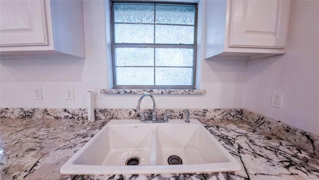 details featuring white cabinets, a sink, and light stone counters
