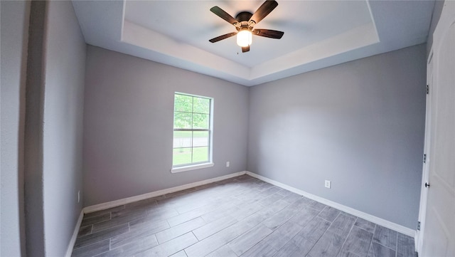 spare room with baseboards, a raised ceiling, wood finished floors, and a ceiling fan