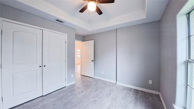 unfurnished bedroom featuring a raised ceiling, light wood-style floors, baseboards, and visible vents
