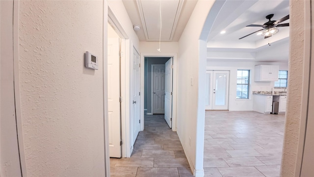 hall with attic access, a textured wall, and baseboards