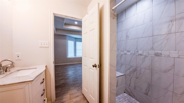 full bathroom with vanity, baseboards, a tile shower, and wood finished floors