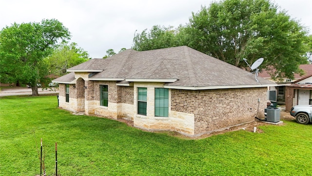 view of side of home with brick siding, roof with shingles, central AC, and a lawn
