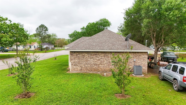 view of home's exterior featuring cooling unit, roof with shingles, a yard, and brick siding