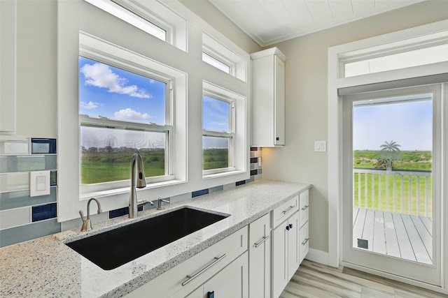4102 Kiva Rd, Galveston, TX 77554 - kitchen with ornamental molding, light stone counters, white cabinets, light wood finished floors, and a sink