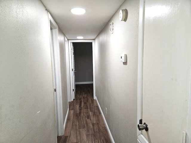 corridor featuring dark wood-type flooring and baseboards