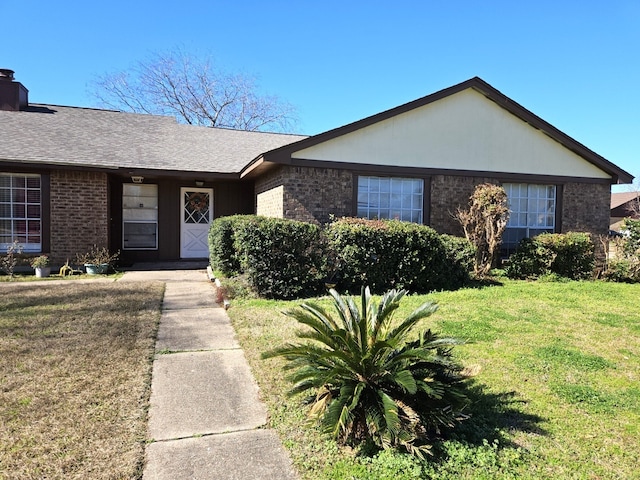 ranch-style home with a front yard, a shingled roof, brick siding, and a chimney