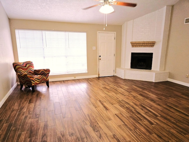 unfurnished room featuring a fireplace, a textured ceiling, a ceiling fan, wood finished floors, and baseboards