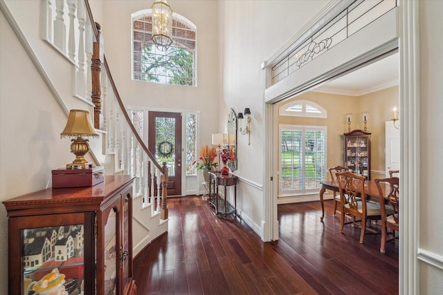 foyer entrance featuring crown molding, stairway, a high ceiling, wood finished floors, and a notable chandelier