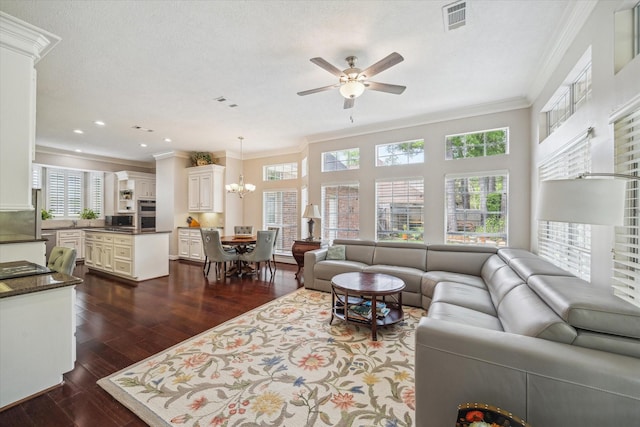 living area with visible vents, ornamental molding, a healthy amount of sunlight, dark wood-style floors, and ceiling fan with notable chandelier