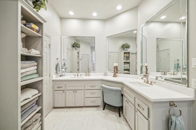 full bath with a sink, double vanity, marble finish floor, and recessed lighting