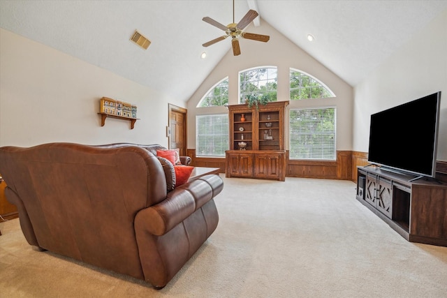 living area featuring high vaulted ceiling, light colored carpet, a ceiling fan, visible vents, and wainscoting