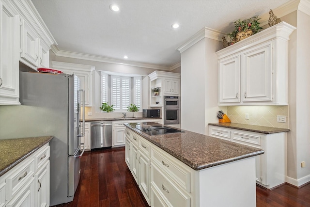 kitchen featuring ornamental molding, dark stone countertops, a center island, dark wood-style flooring, and stainless steel appliances