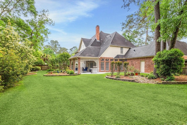 back of house with a patio area, brick siding, a lawn, and a chimney