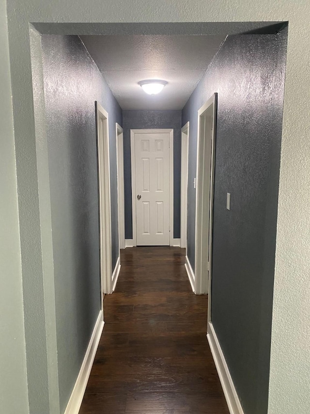 hall featuring a textured wall, dark wood-style flooring, a textured ceiling, and baseboards