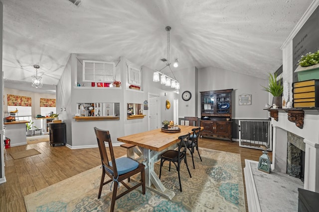 dining space featuring vaulted ceiling, wood finished floors, a textured ceiling, a fireplace with raised hearth, and baseboards
