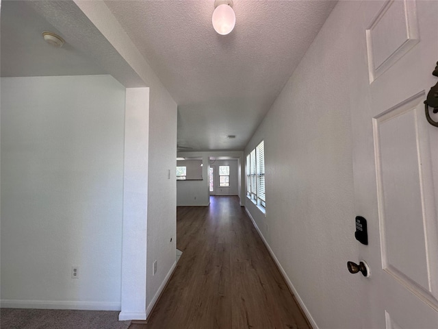 corridor featuring wood finished floors, baseboards, and a textured ceiling