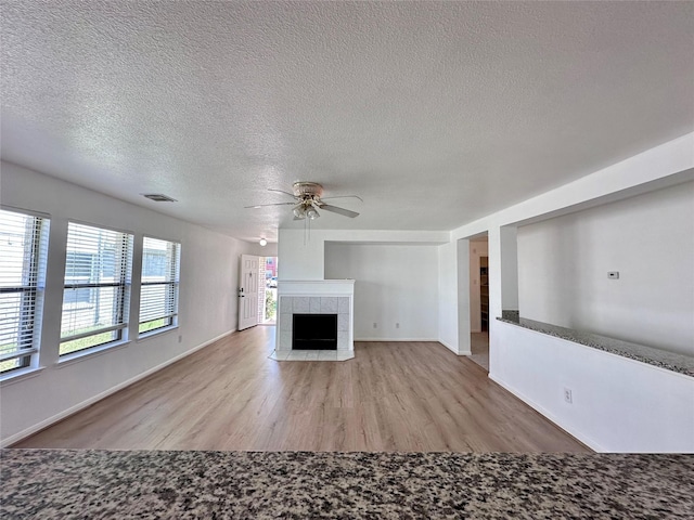 unfurnished living room with a textured ceiling, wood finished floors, visible vents, and ceiling fan