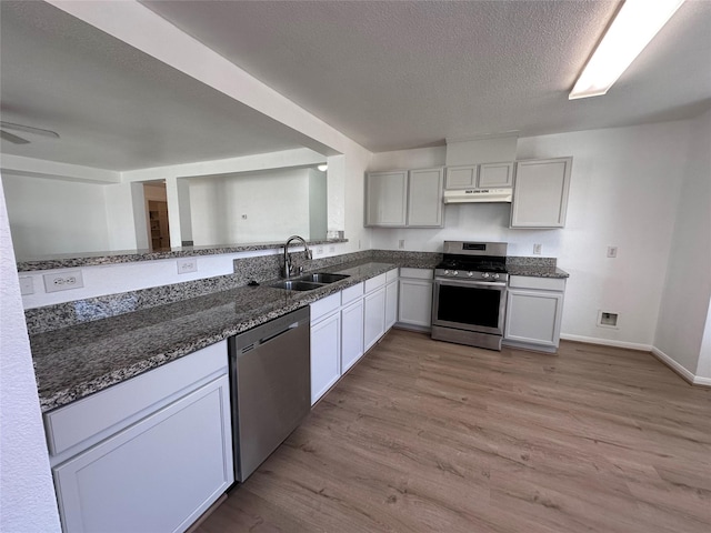 kitchen with stainless steel appliances, light wood-style flooring, a sink, dark stone counters, and under cabinet range hood