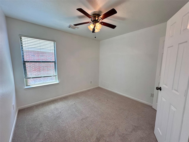 carpeted spare room with visible vents, a ceiling fan, and baseboards