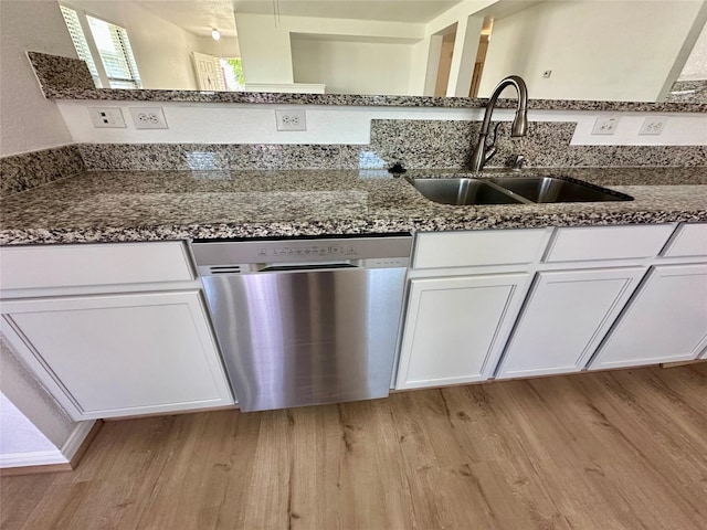 kitchen featuring light wood-style floors, dark stone countertops, stainless steel dishwasher, and a sink