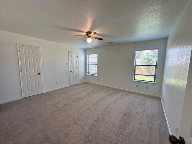 unfurnished room with light colored carpet, a wealth of natural light, a ceiling fan, and visible vents