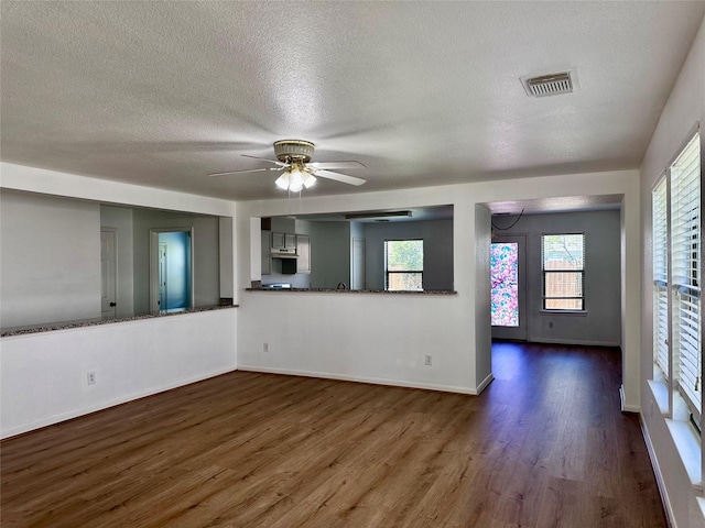 unfurnished living room with a textured ceiling, dark wood-style floors, and a wealth of natural light