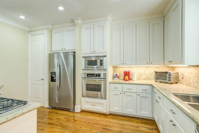 kitchen with white cabinets, appliances with stainless steel finishes, light wood-style flooring, decorative backsplash, and a toaster
