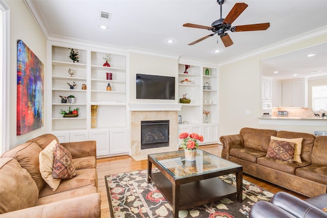 living room featuring a ceiling fan, visible vents, crown molding, a fireplace, and light wood-style floors