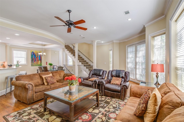 living room with visible vents, ornamental molding, decorative columns, wood finished floors, and ceiling fan with notable chandelier