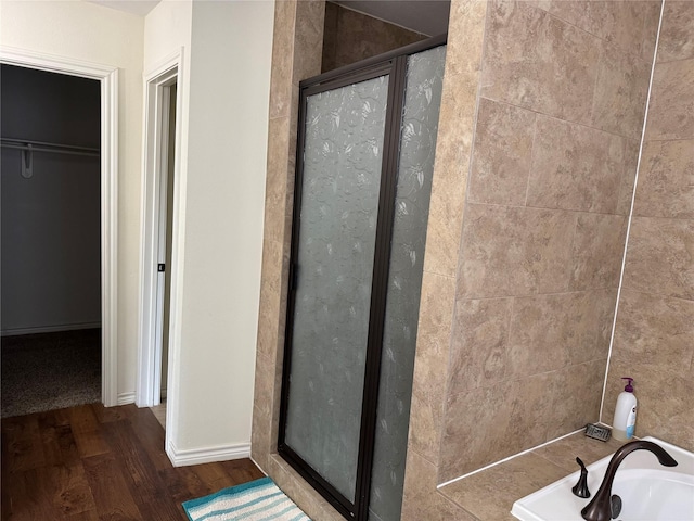 full bath with a walk in closet, a washtub, a shower stall, and wood finished floors
