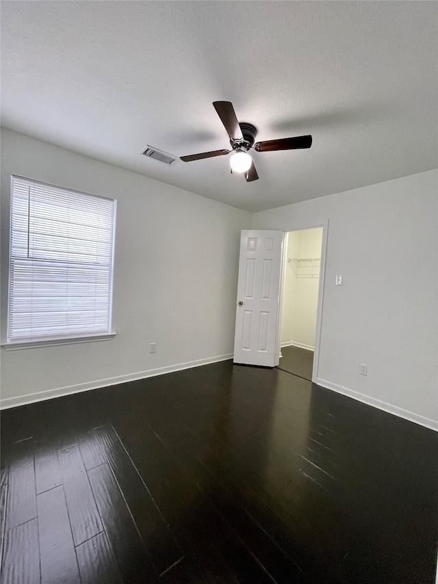 spare room featuring ceiling fan, baseboards, dark wood-style floors, and visible vents