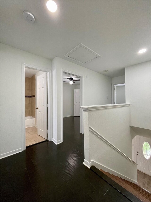 hallway with an upstairs landing, baseboards, attic access, and wood finished floors