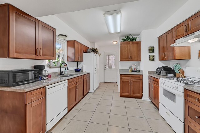kitchen with white appliances, a sink, under cabinet range hood, light tile patterned flooring, and plenty of natural light