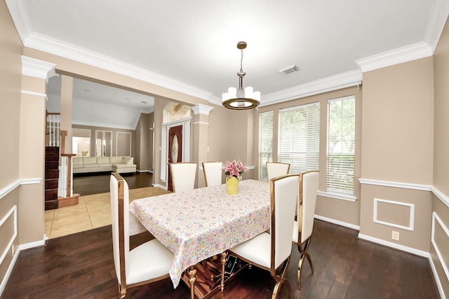 dining space featuring dark wood finished floors, crown molding, baseboards, a chandelier, and ornate columns