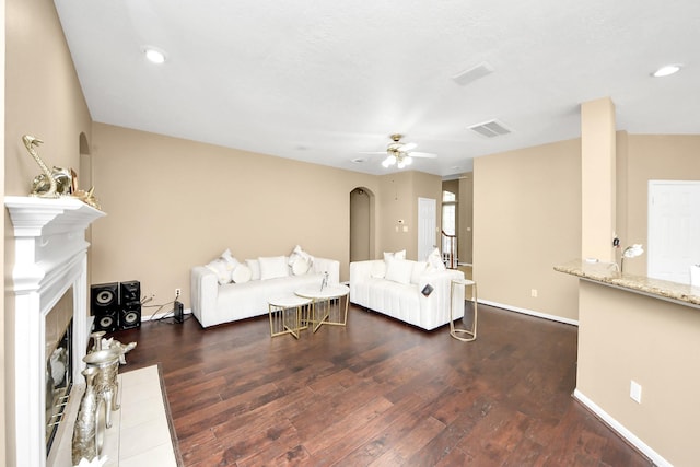 living room with a fireplace, dark wood-type flooring, ceiling fan, arched walkways, and baseboards
