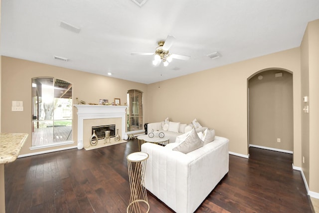 living room featuring ceiling fan, arched walkways, dark wood finished floors, and a tile fireplace