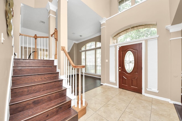 foyer with stairs, light tile patterned floors, baseboards, ornamental molding, and a towering ceiling