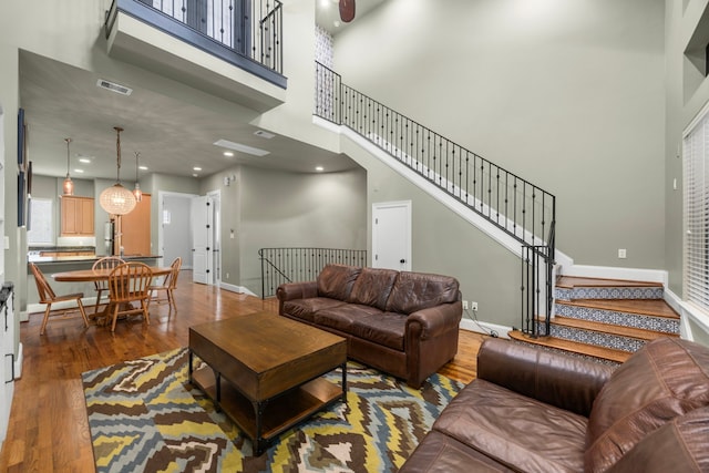 living area with visible vents, stairs, a towering ceiling, wood finished floors, and baseboards