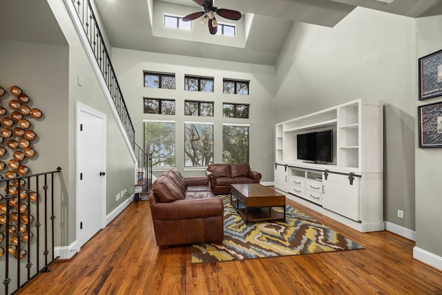 living room featuring a ceiling fan, a towering ceiling, wood finished floors, stairway, and baseboards