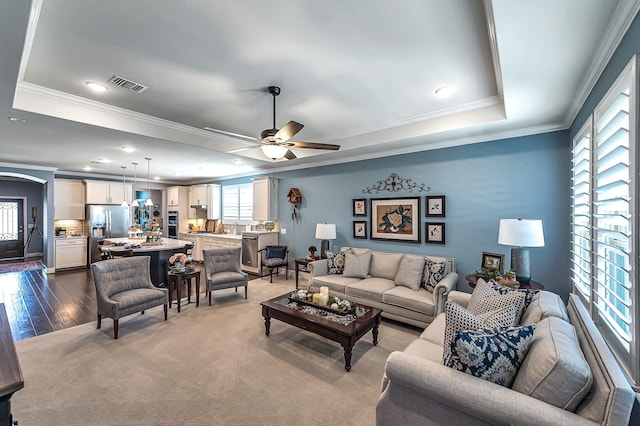 living area featuring crown molding, visible vents, ceiling fan, and a raised ceiling