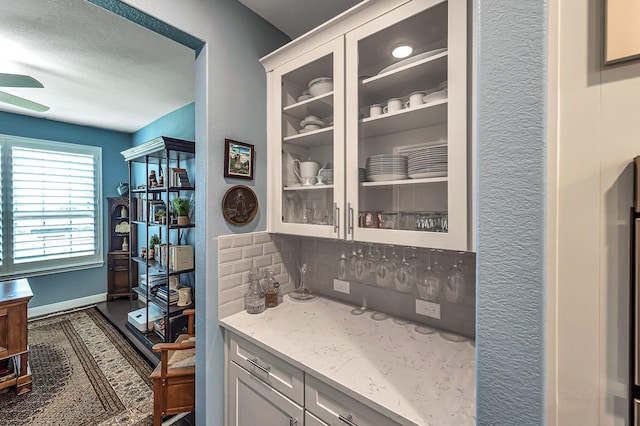 bar with a textured wall, ceiling fan, baseboards, and backsplash