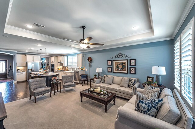 living room featuring crown molding, visible vents, ceiling fan, and a raised ceiling