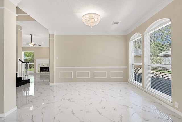empty room featuring a decorative wall, ceiling fan with notable chandelier, ornamental molding, visible vents, and marble finish floor