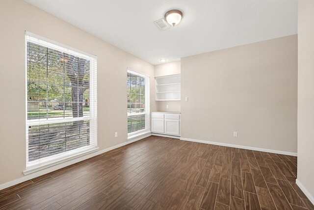 empty room with dark wood-type flooring, visible vents, and baseboards