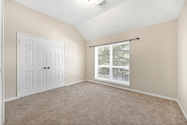 unfurnished bedroom featuring visible vents, baseboards, a closet, vaulted ceiling, and carpet flooring