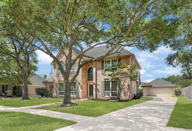 traditional-style house with a garage, a front yard, fence, brick siding, and concrete driveway