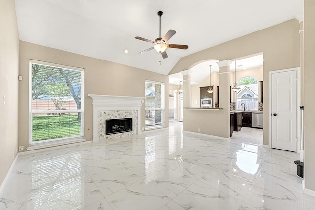unfurnished living room featuring baseboards, lofted ceiling, decorative columns, marble finish floor, and ceiling fan