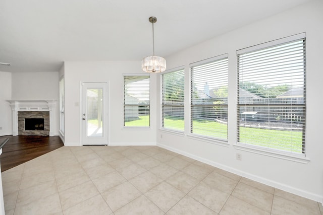 unfurnished dining area featuring a chandelier, a fireplace, baseboards, and tile patterned floors